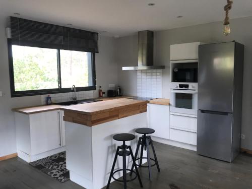 La cuisine est équipée d'un comptoir, d'un réfrigérateur et de tabourets. dans l'établissement Maison 3 chambres 900 m plage, à Lacanau