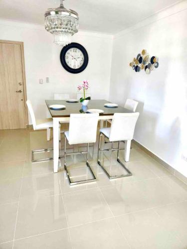 a dining room table with white chairs and a clock on the wall at Residencial El Molino 1 - 3 bedrooms 2 bathrooms in Concepción de La Vega