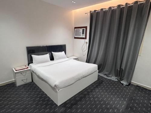 a bedroom with a white bed and a gray curtain at Madain Al Baraka Suites أجنحة مدائن البركة in Medina