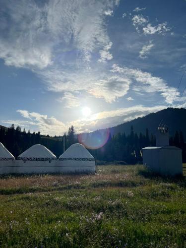 a group of tents in a field with the sun in the sky at Karkyra Yurt Glamping in Sarytëbë