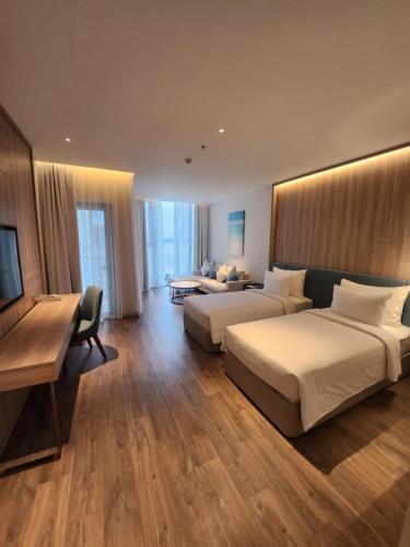 a hotel room with two beds and a desk at A La Carte Ha Long Bay Managed by TASECO in Ha Long