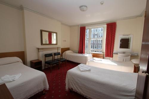a hotel room with three beds and a fireplace at Ridgemount Hotel in London
