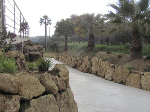 a stone wall next to a walkway with palm trees at Folco Studio Apartment in Piazza Armerina
