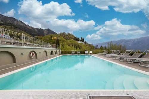 a large swimming pool with chairs and mountains in the background at Residence La Villa Diamante in Tignale