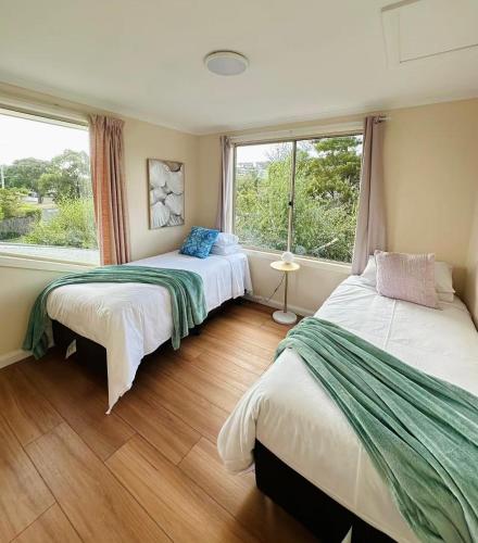 two beds in a room with two windows at Beach House 3 mins Walk Bellerive Beach, Hobart in Bellerive