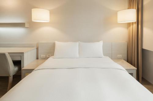 a bedroom with a large white bed and a desk at Kindness Hotel - Jhandong Jiuru Branch in Kaohsiung