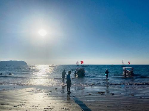 people standing on the beach with boats in the water at Oliver`s Laguna ECO Lodge Hotel in Ngapali