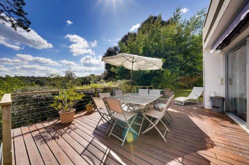 une terrasse en bois avec une table, des chaises et un parasol dans l'établissement La maison des Pins au Pyla sur mer, à La Teste-de-Buch