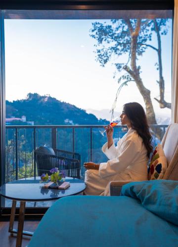 a woman sitting on a balcony drinking a glass of wine at Perfectstayz Premium Westend at Mall Road in Mussoorie