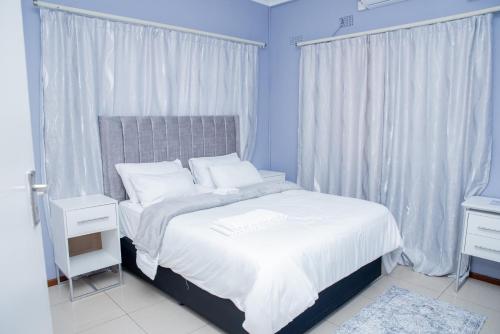 a bedroom with a bed with white sheets and curtains at Avenue Inn in Gaborone