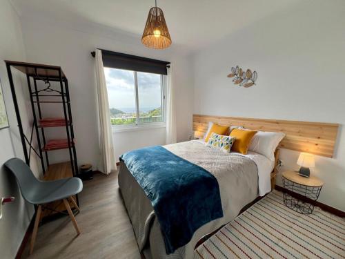Un dormitorio con una cama y una silla y una ventana. en Vila Mandala, en Ponta Delgada