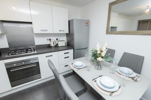 a white kitchen with a dining table and appliances at Manchester Cityside Deluxe Stay - 3 Bedroom House Great for Family with Free Parking & Garden in Manchester