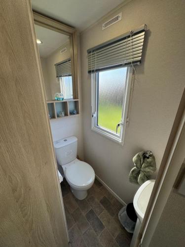 a small bathroom with a toilet and a window at Meadowside Caravan Hire Haven Kent Coast in Allhallows