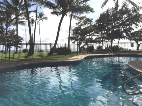 a swimming pool with palm trees in front of a fence at Hotel Coral Reef in Kapaa