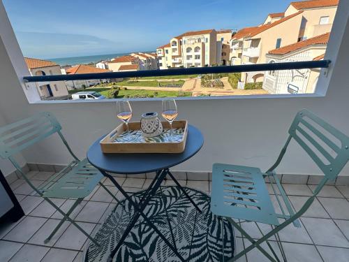 une table avec deux chaises et des verres à vin sur un balcon dans l'établissement T2 neuf- Balcon-Vue privilégiée Océan - Sud Ouest, à Les Sables-dʼOlonne