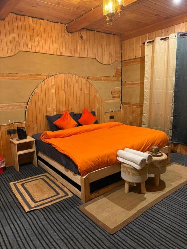 a bedroom with an orange bed with a wooden wall at Kath Kuni Cafe & Stay Shangarh in Shangarh