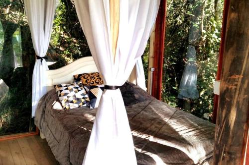 a bed in a room with a window with curtains at Casa de Vidro na Mata, com Lago, cachoeira, caiaque, Stand up, escorregador no lago in Itatiba