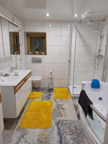 a bathroom with a tub and a shower and yellow rugs at Ferienwohnung Unterm Rappenfels in Hinterweidenthal