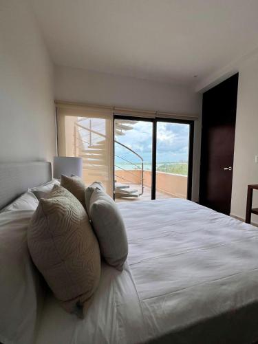 a bedroom with a bed with pillows and a balcony at Penthouse Navela 405 by Cercana in Telchac Puerto