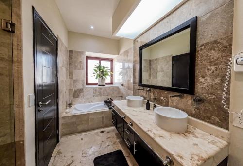 Un baño con dos lavabos, una bañera y un espejo grande. en Beachfront Chic at El Faro Resort, en Playa del Carmen