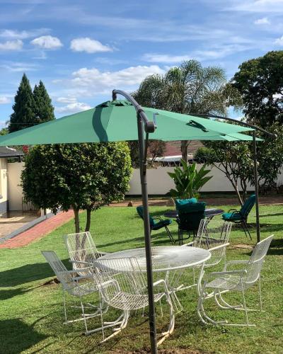 a table and chairs under a green umbrella at Mongi Guest House in Harare