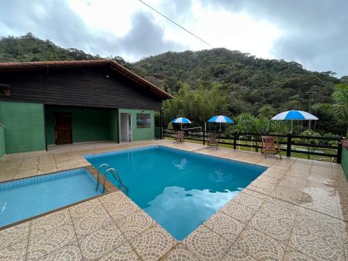 a swimming pool in front of a house with umbrellas at Sítio recanto toca da onça in Nova Friburgo