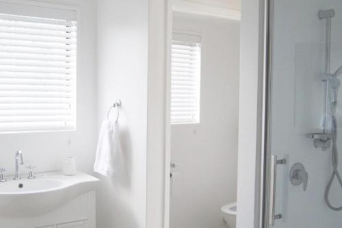 a white bathroom with a sink and a shower at Daisy Harbour View - Waterfront! in Raglan