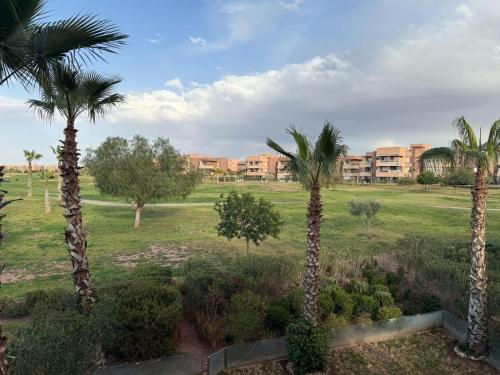 a group of palm trees in a field with a building at Appartement Prestigia Agate résidence avec piscine in Marrakech