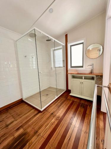 a glass shower in a bathroom with a wooden floor at Alexander's Cottage, Pebbly Beach in East Lynne
