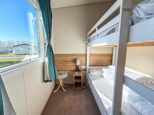 Un dormitorio con dos literas y una ventana. en Beautiful Caravan With Decking At Manor Park, Hunstanton Ref 23098T, en Hunstanton