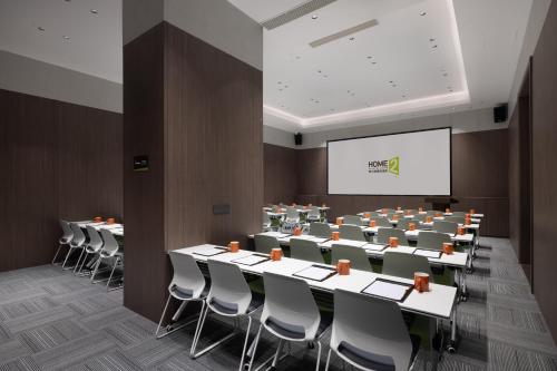 una sala de conferencias con mesas y sillas y una pantalla de proyección en Home2 Suite by Hilton Yiwu World Trade Center, en Yiwu