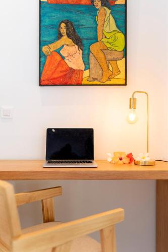 a laptop sitting on a desk with a painting on the wall at Iaorana Lodge - Moorea in Temae