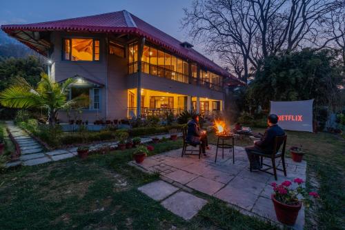 two people sitting around a fire in front of a house at SaffronStays Casa Octavia in Bhīm Tāl