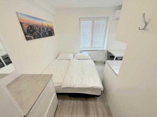 a white bedroom with a bed and a desk at Krásny byt - garzonka v Novom meste in Koliba