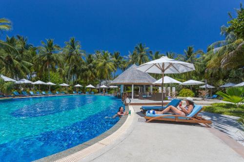 a pool at a resort with people laying on chairs and umbrellas at Bandos Maldives in North Male Atoll