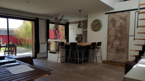 une cuisine avec un bar avec des tabourets et une horloge sur le mur dans l'établissement Maison avec 3 appartements à 5min de la plage sud, à Lacanau