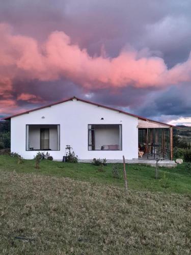a white house in a field with a cloudy sky at Finca Siberia, Sisga in Tilatá