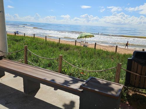 a wooden bench sitting next to a beach with an umbrella at Casa de Praia em Jacaraipe soneto do Mar in Serra