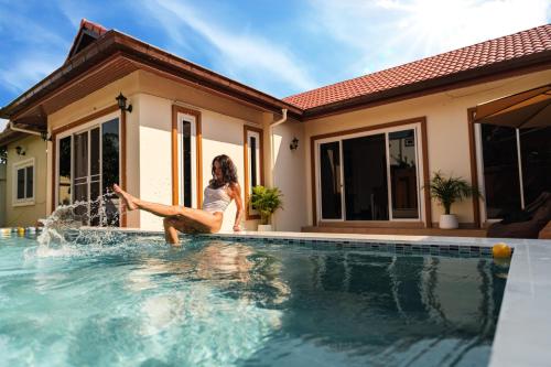 a woman sitting on the edge of a swimming pool in front of a house at Queen Massarossa Pool Villa Pattaya-25 in Pattaya