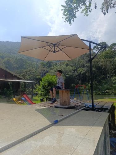 a boy sitting on a bench under an umbrella at Refúgio Atlântico in Mogi das Cruzes