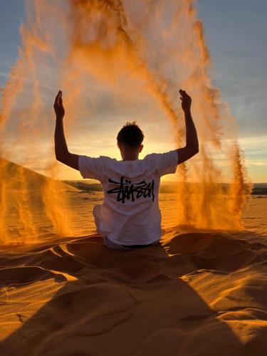 a man sitting in the desert with his arms in the air at Merzouga wild Camp in Merzouga