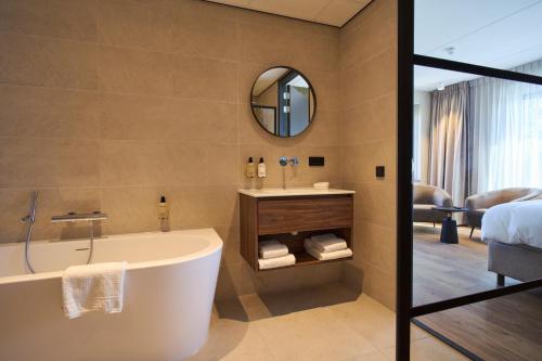 a bathroom with a tub and a bed and a mirror at Eilandhotel Texel - Nieuw geopend hotel in De Cocksdorp