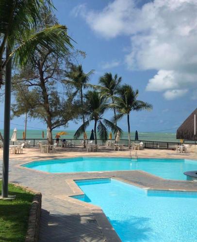 a swimming pool with palm trees and the ocean at Flat Gold Beach in Recife
