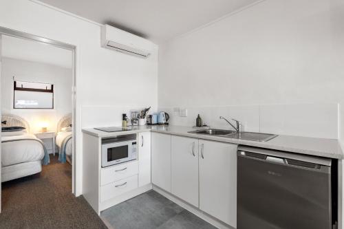 a white kitchen with a sink and a dishwasher at Orewa Beachcomber in Orewa