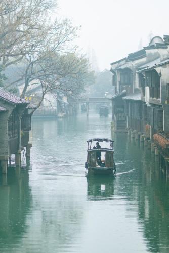 a boat traveling down a river with houses on it at Wuzhen Xizha Slow Life Riverside Inn in Wujiaqiao