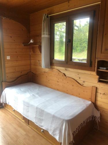 a bed in a log cabin with a window at La Roulotte d'Alcas in Saint-Jean-et-Saint-Paul