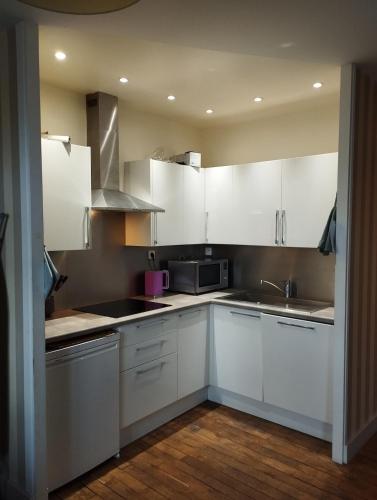 une cuisine avec des armoires blanches, un évier et un micro-ondes dans l'établissement Appartement au cœur de Poitiers, à Poitiers