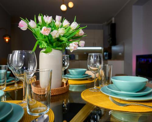 a table with plates and a vase of pink flowers at Marijas Apartment with Comfort for 5 in Rīga