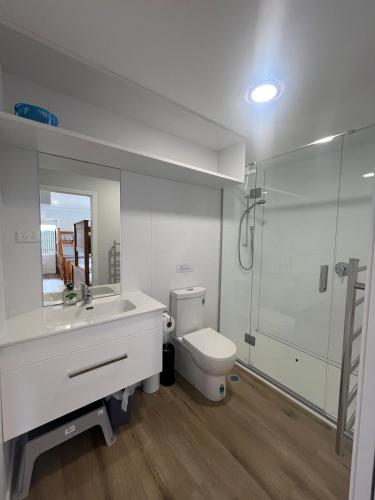 a white bathroom with a toilet and a shower at Waipu Cove Surf Cabin in Waipu