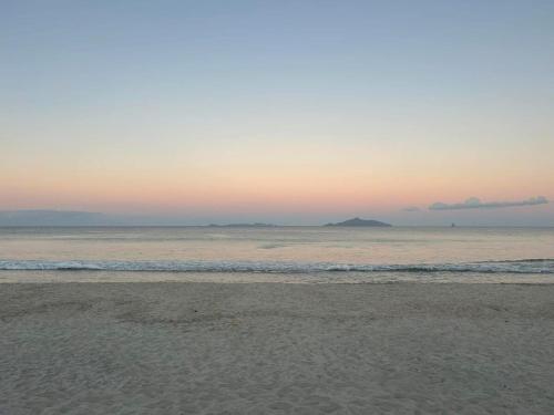 a beach with an island in the ocean at sunset at Waipu Cove Surf Cabin in Waipu